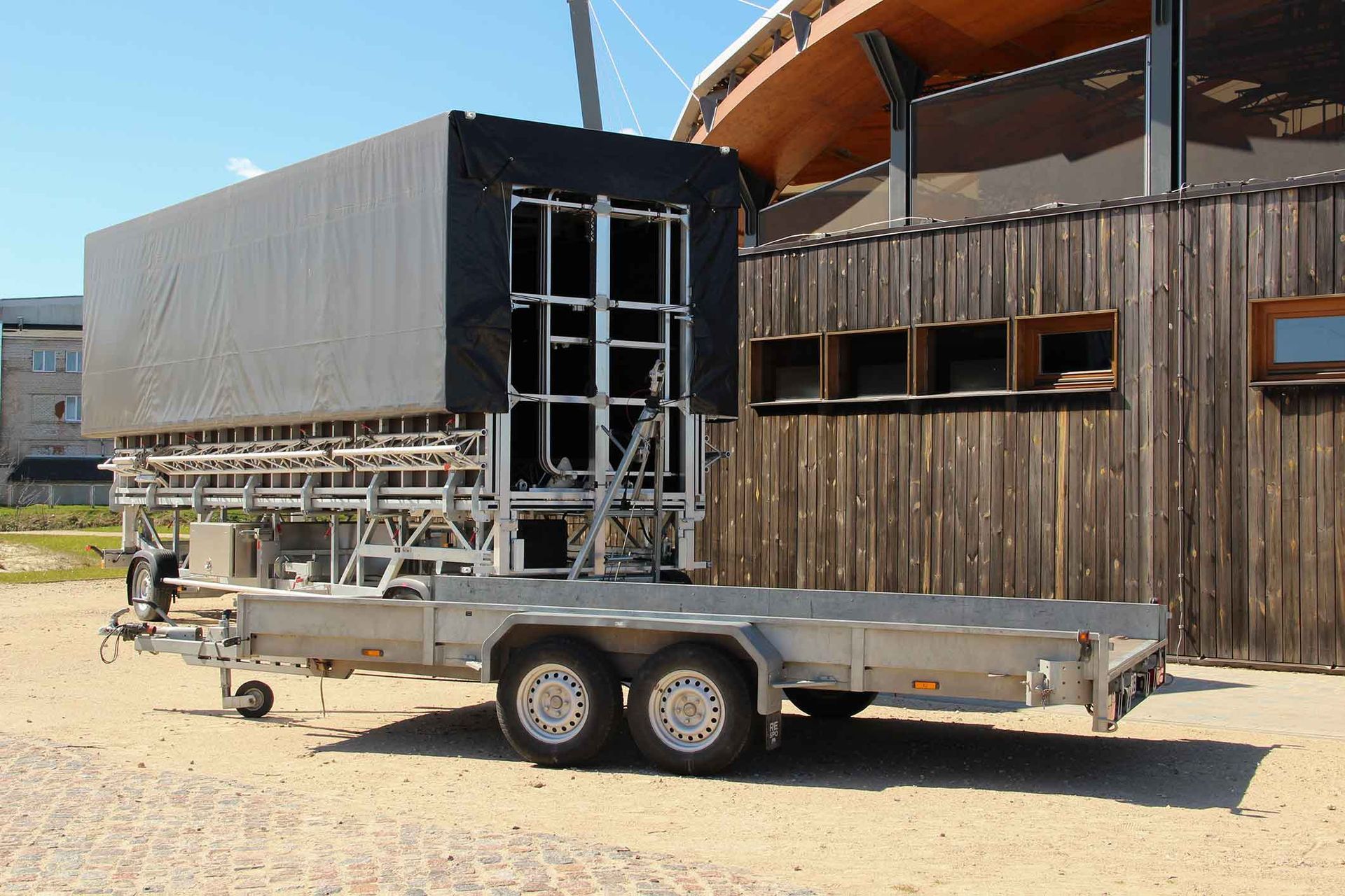 A large black structure on a trailer, next to a wooden building.