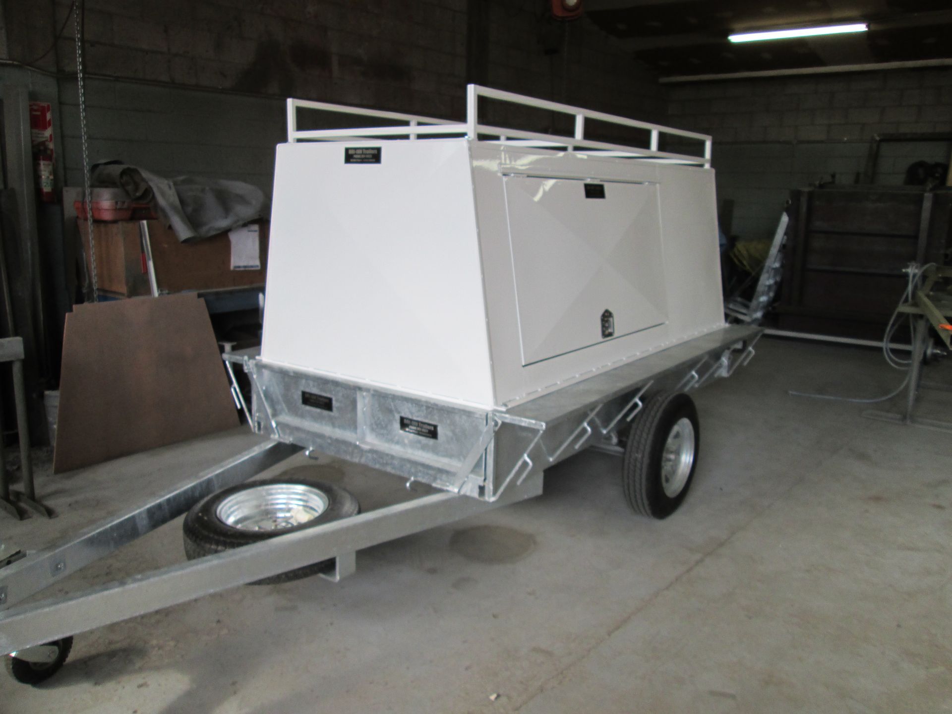 Black and silver rectangular structure on a trailer, next to a wooden building and stadium-like structure.