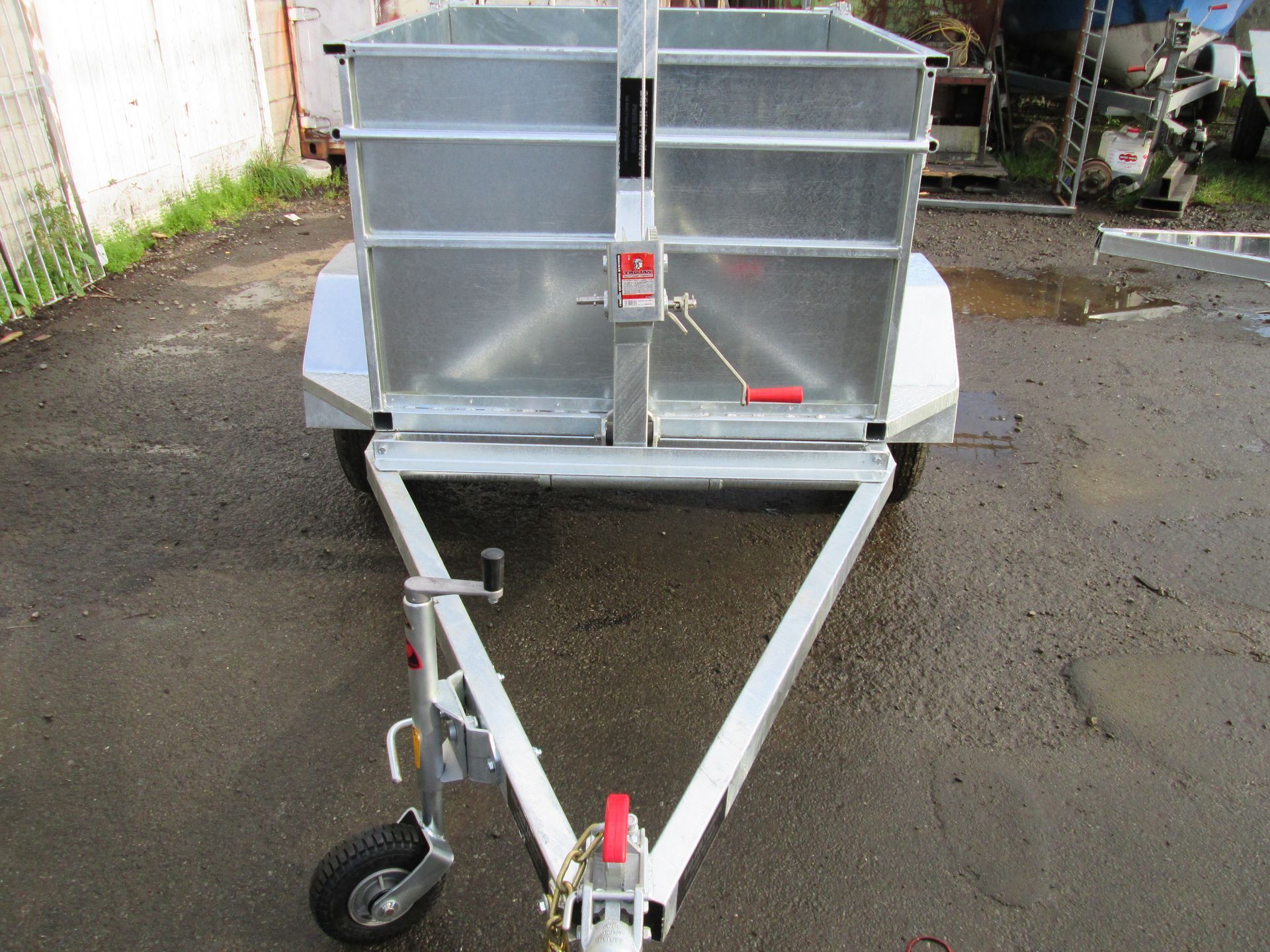Galvanized utility trailer with two bins and a hitch, parked on a wet surface.