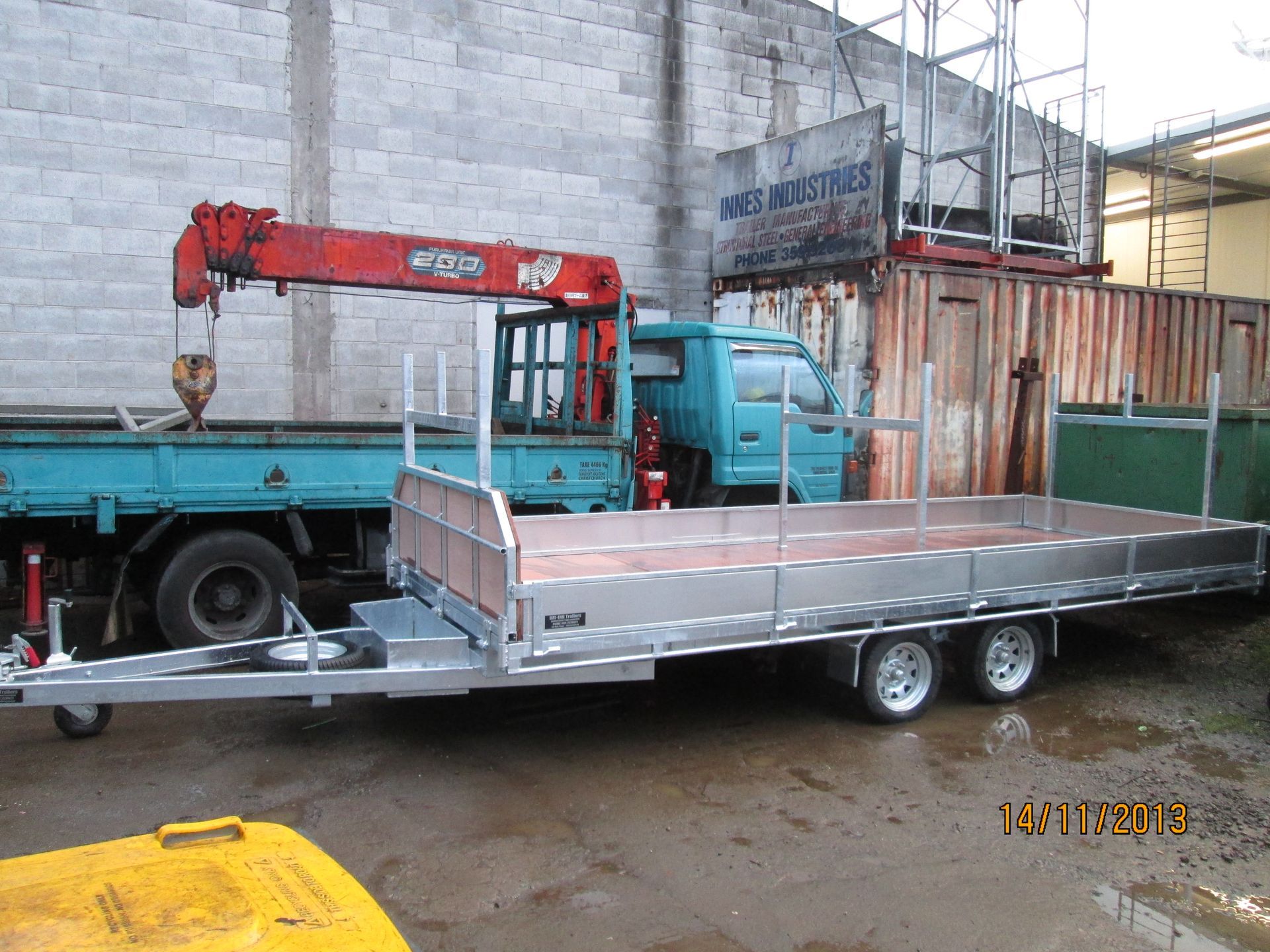 Flatbed trailer with a light blue truck and crane in the background.
