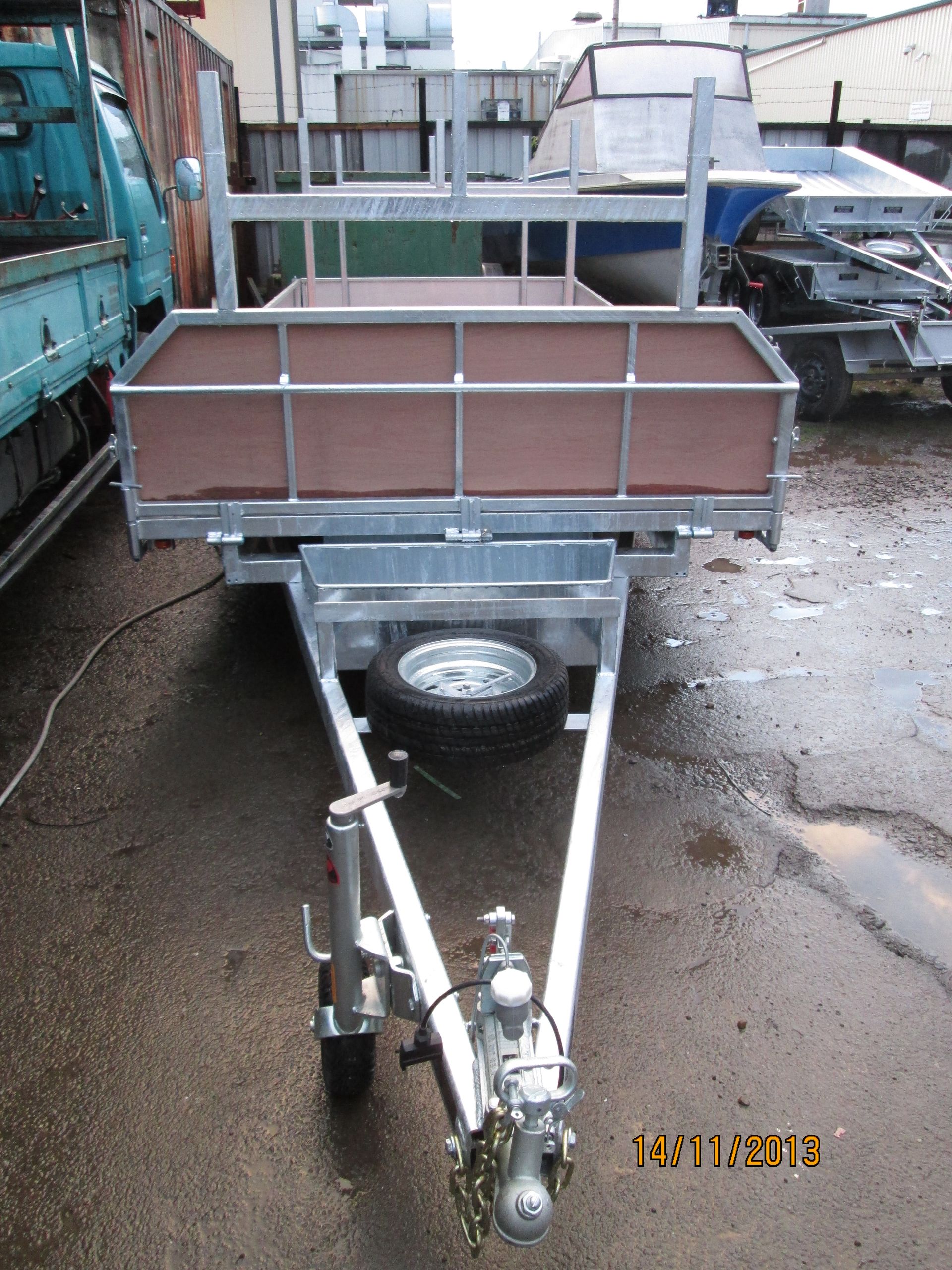 Galvanized utility trailer with brown side panels, spare tire, and hitch, outdoors.