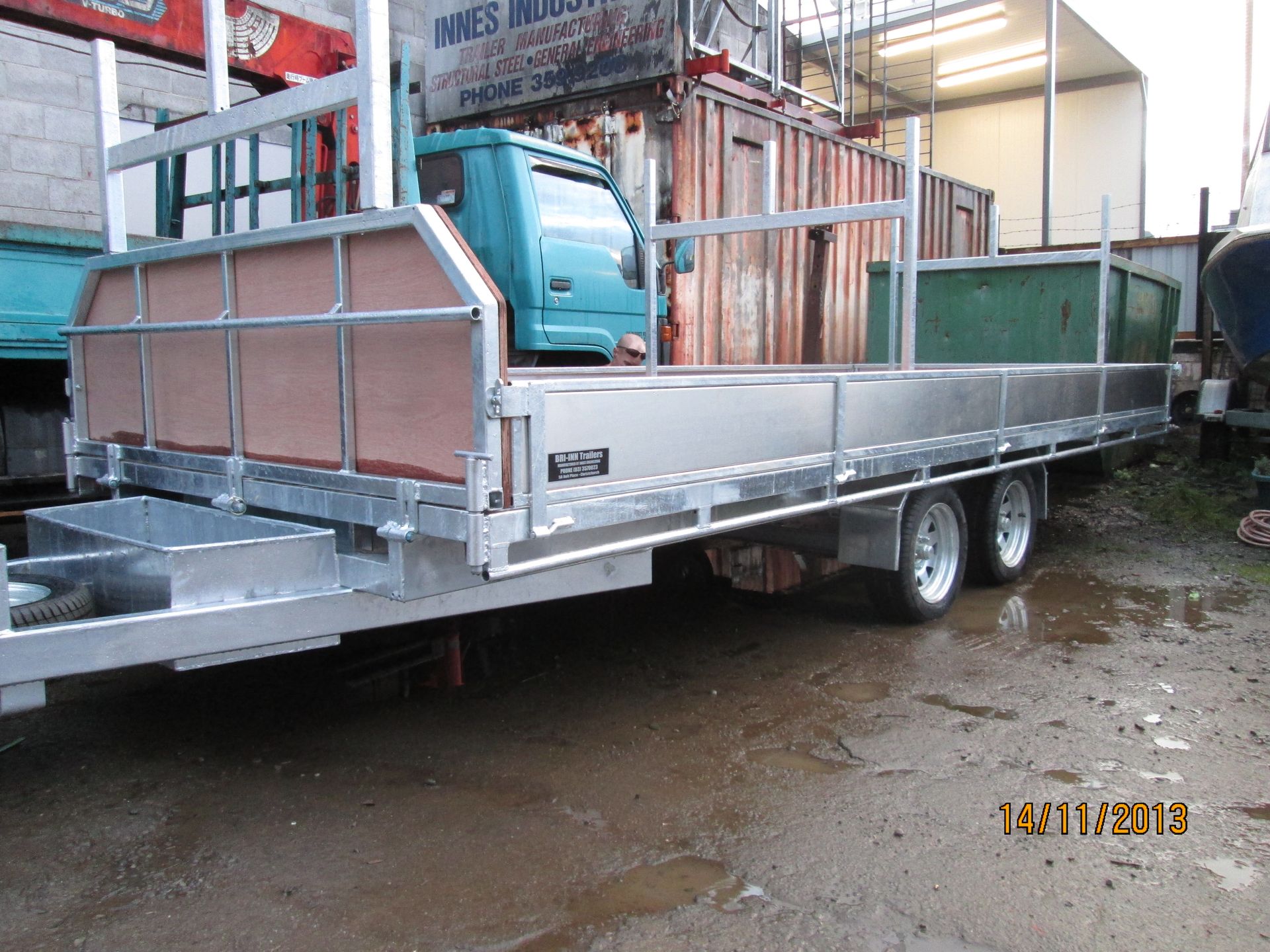 Aluminum trailer with a light blue cab-over truck bed and green container in an industrial setting.