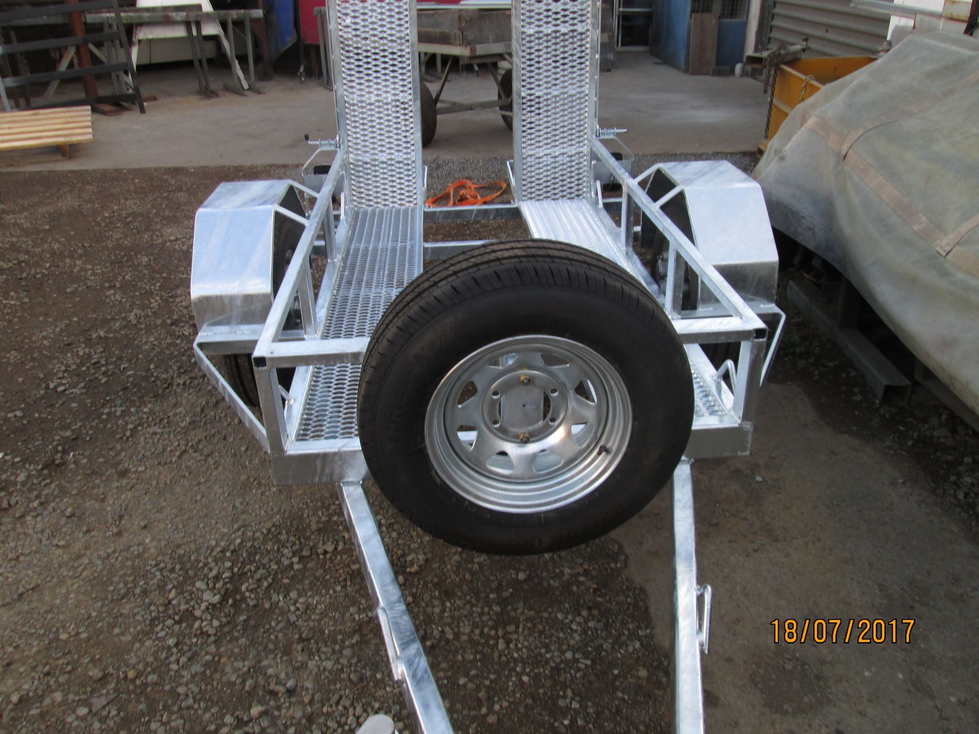 Silver motorcycle trailer with a spare tire.