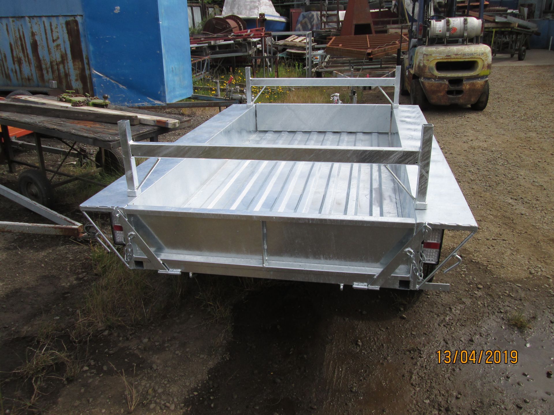 Galvanized steel utility trailer with spare tire and toolbox on a gravel surface.