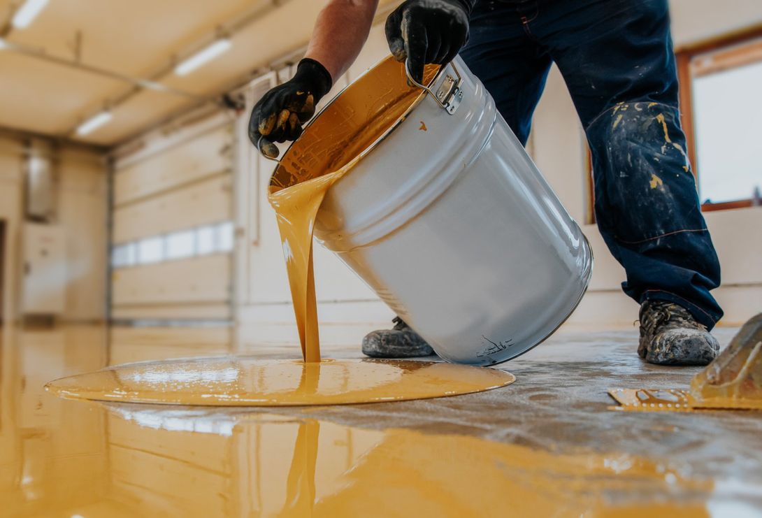 Worker applying a yellow epoxy resin bucket on floor.