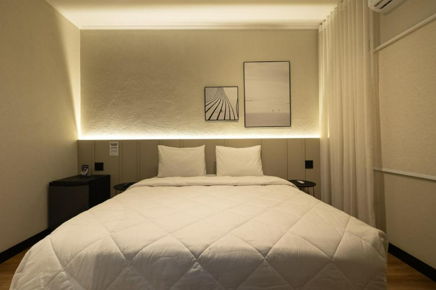 Quarto com uma cama grande, dois travesseiros e obras de arte na parede. Iluminação suave.