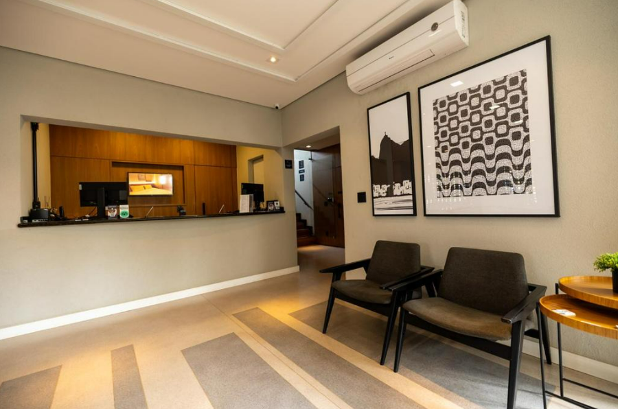 Hall de entrada com balcão de recepção, cadeiras, obras de arte e ar condicionado.