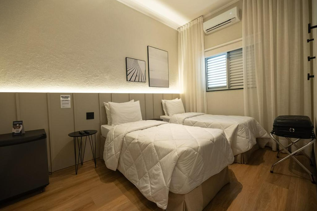 Um quarto de hotel com duas camas de solteiro, paredes claras e piso de madeira.