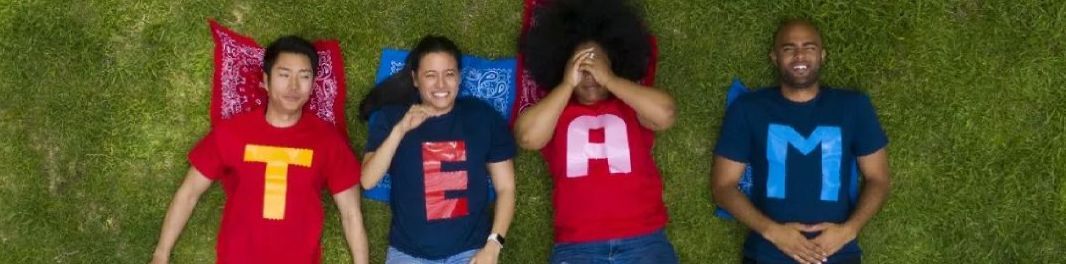 four adults lying on grass each in t-shirt with a letter that spells out team