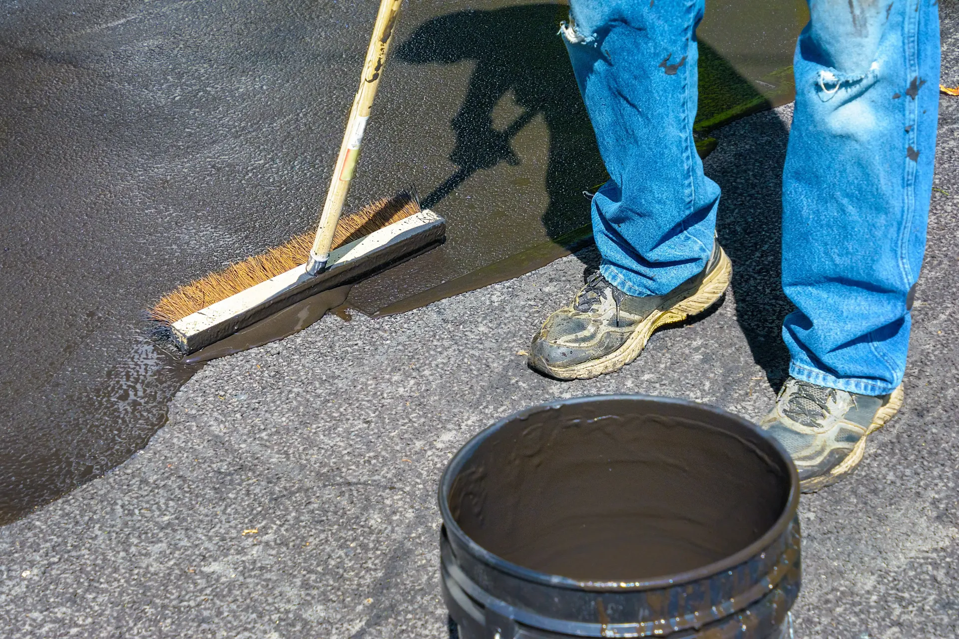 Man spreads tar sealant on old asphalt.