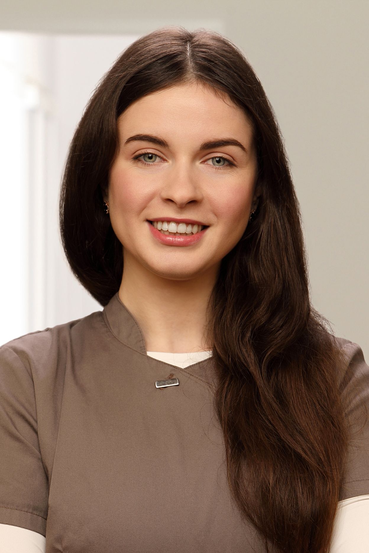 Eine Frau in einem braunen Kasack und einem weißen Rollkragenpullover lächelt in die Kamera.