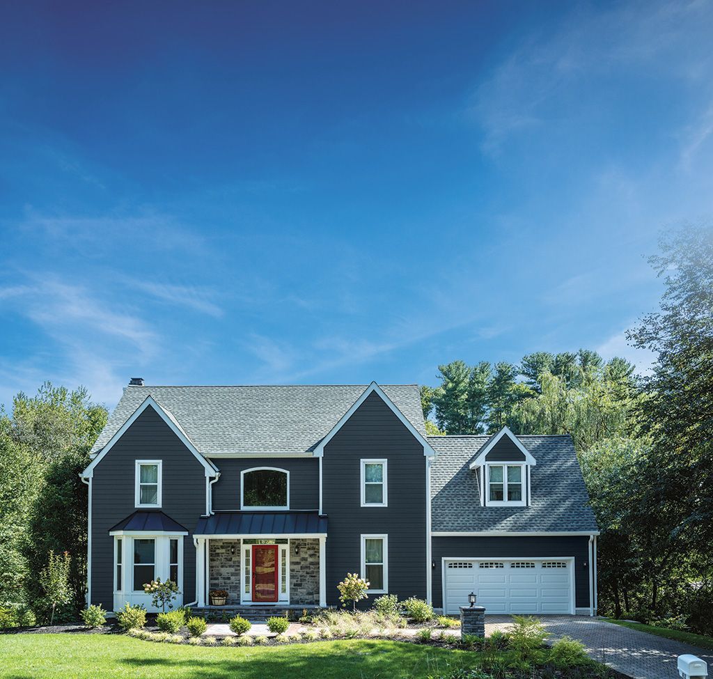 A two-story dark gray house with a red front door, stone accents, and an attached garage set against a blue sky.