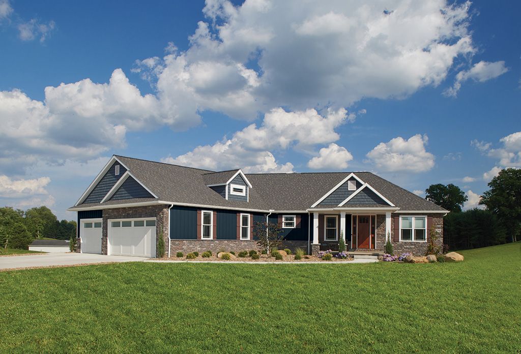 A modern, single-story house with dark blue siding, stone accents, and a large white garage, set in a grassy field.
