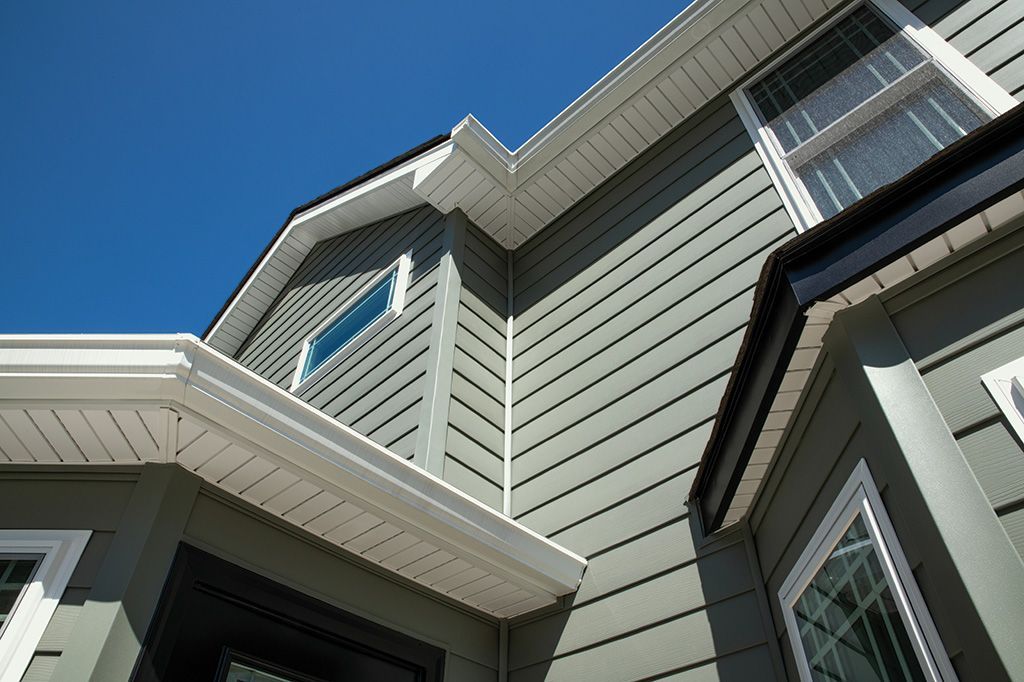 Low-angle view of a modern house exterior with dark gray horizontal siding, white trim, and a bright blue sky.