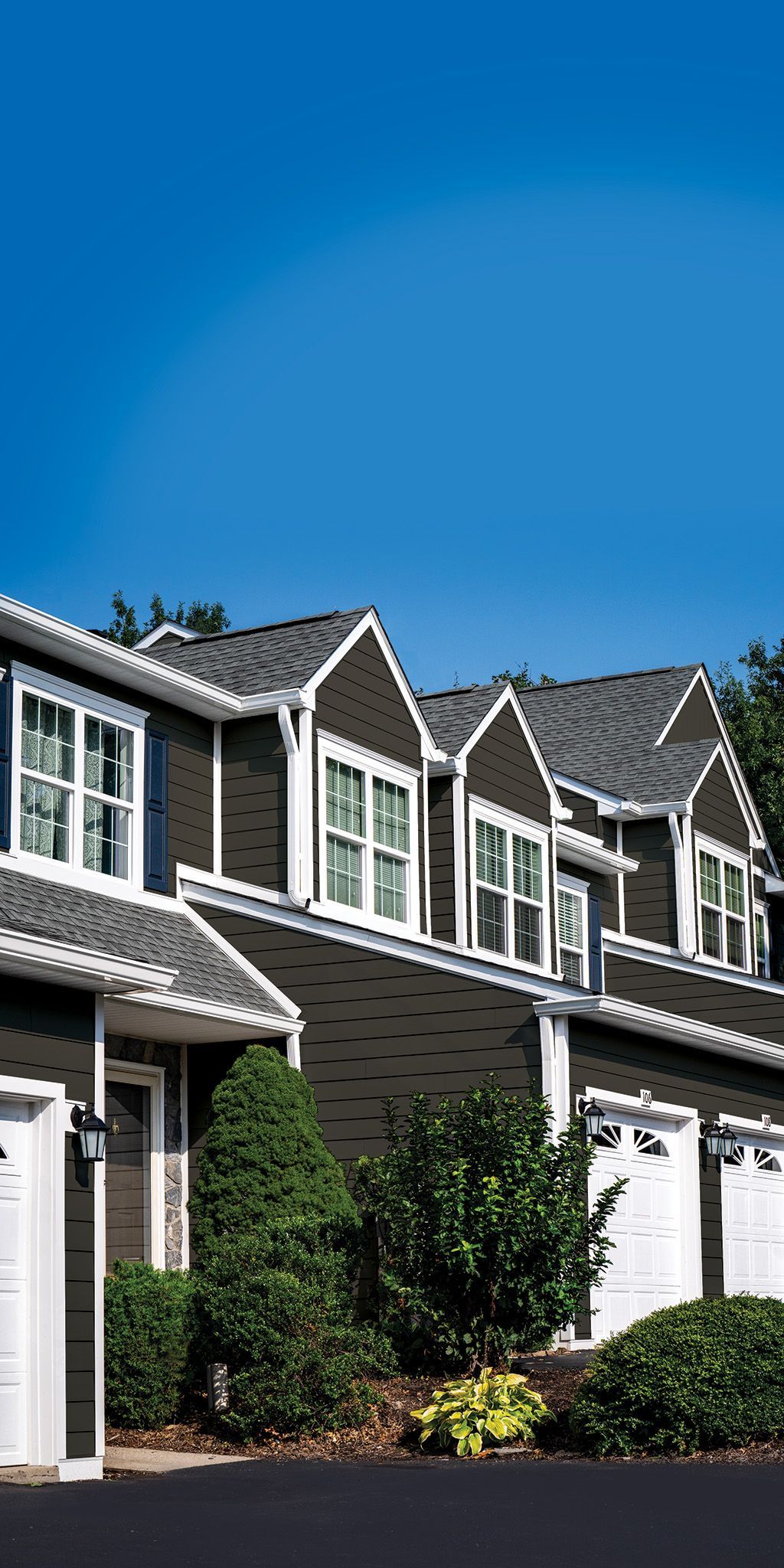A row of dark-sided townhomes with white trim and multi-gabled roofs under a clear blue sky.