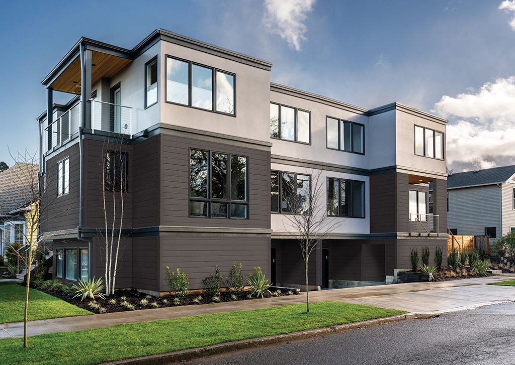 A modern three-story apartment building with gray and white exterior cladding and a ground-level garage entrance.
