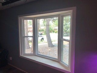A large window in a room with a view of trees and a street.