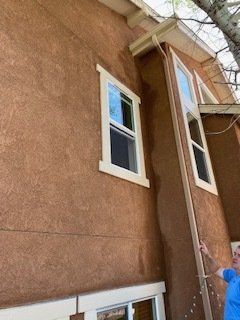A man is standing in front of a brown house with two windows.