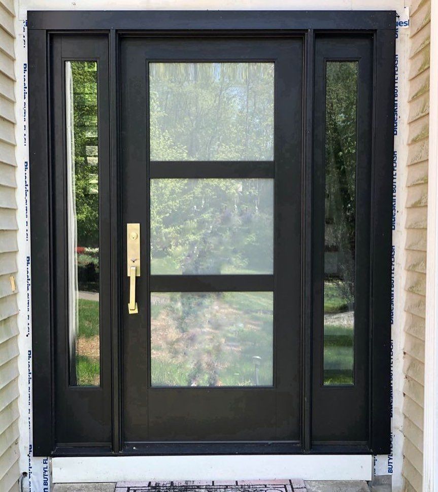 A black front door with three windows and a gold handle on a house.