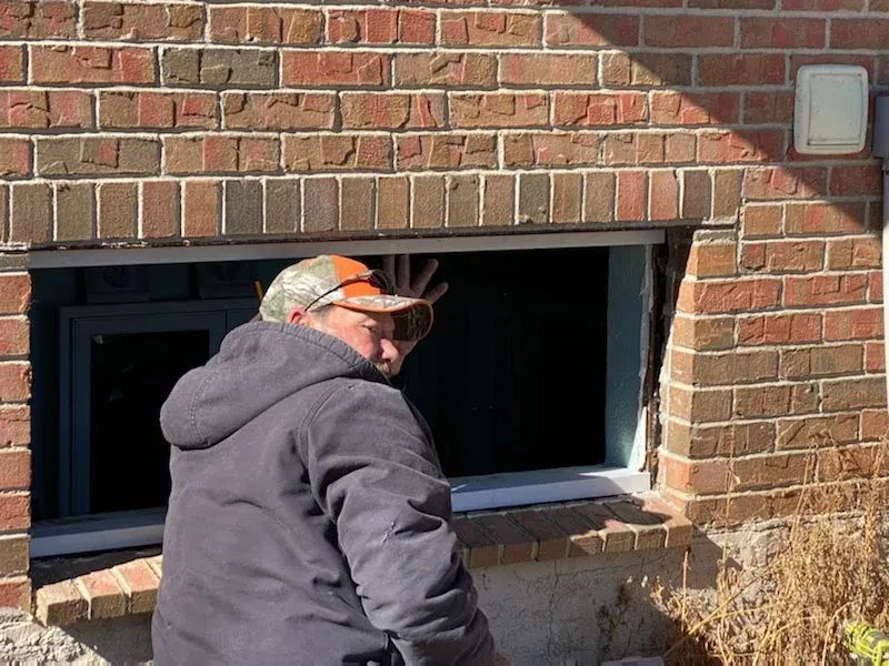 A man is standing in front of a brick wall looking out of a window.