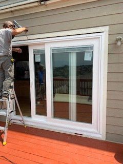 A man is standing on a ladder installing a sliding glass door.