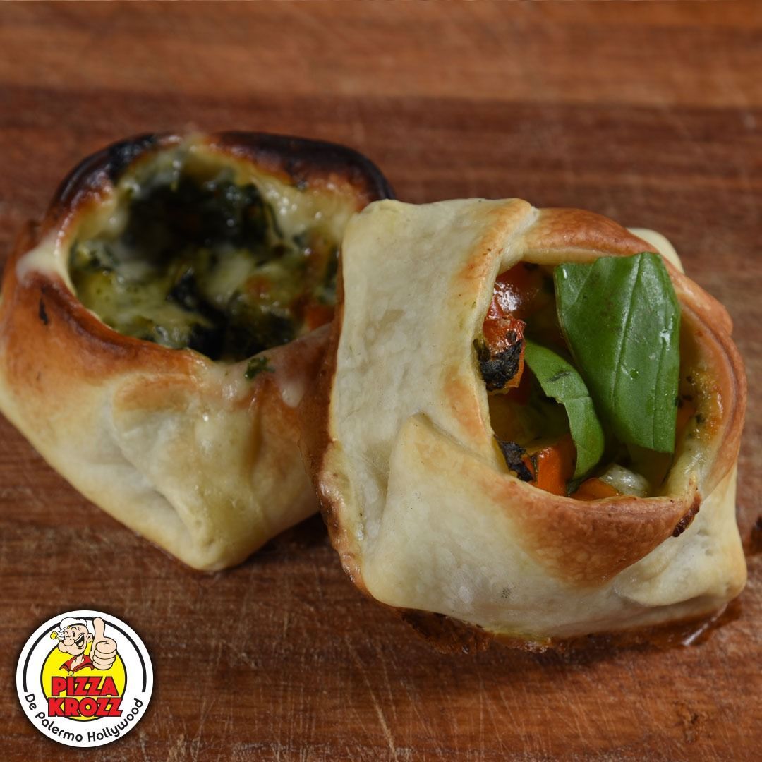 Dos pequeños pasteles salados de color marrón dorado con centros abiertos rellenos de verduras verdes