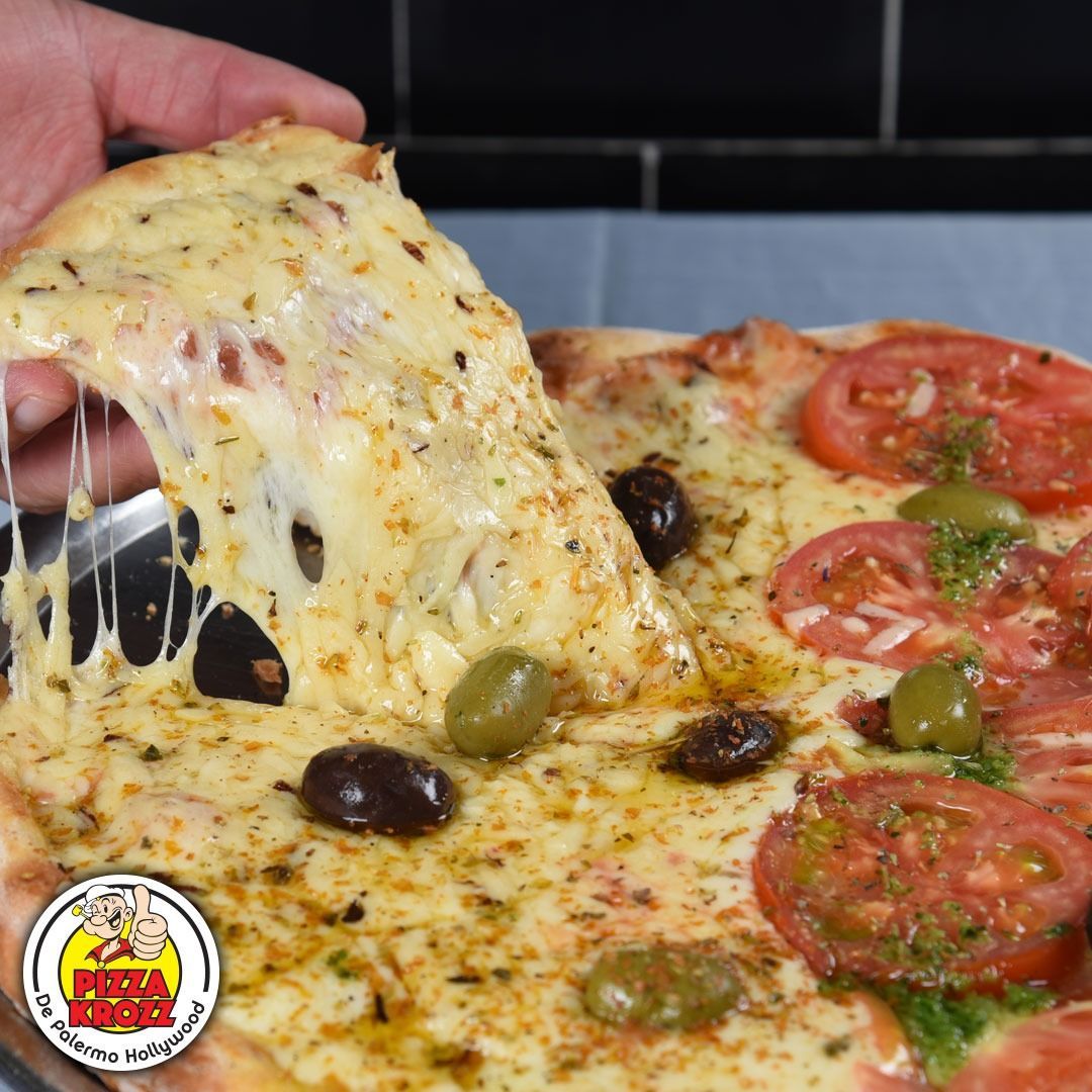 Se está levantando una porción de pizza caliente con queso, tomates y aceitunas
