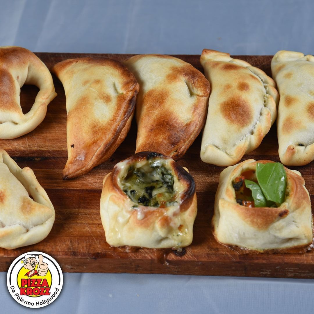 Una tabla de madera con varias empanadas doradas y pasteles salados abiertos, con el logotipo de Pizza King debajo.