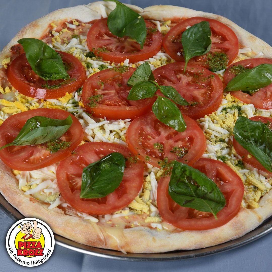 Una pizza cubierta con rodajas de tomate fresco y hojas de albahaca, con un logotipo en la esquina.