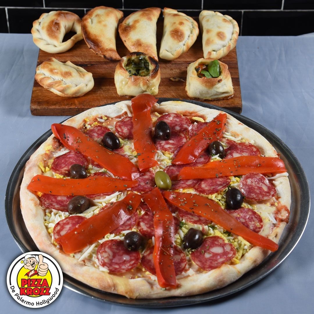 Una pizza grande de pepperoni y pimiento rojo asado en una bandeja de metal, con una tabla de madera
