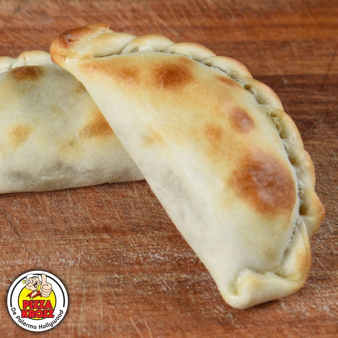 Dos empanadas horneadas y doradas se encuentran sobre una tabla de cortar