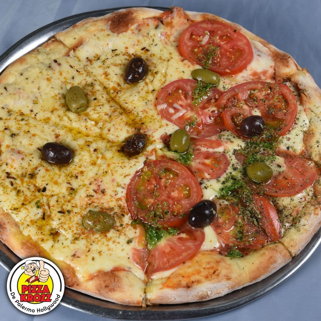 Una pizza mitad queso y mitad tomate, cubierta con aceitunas verdes y negras y hierbas