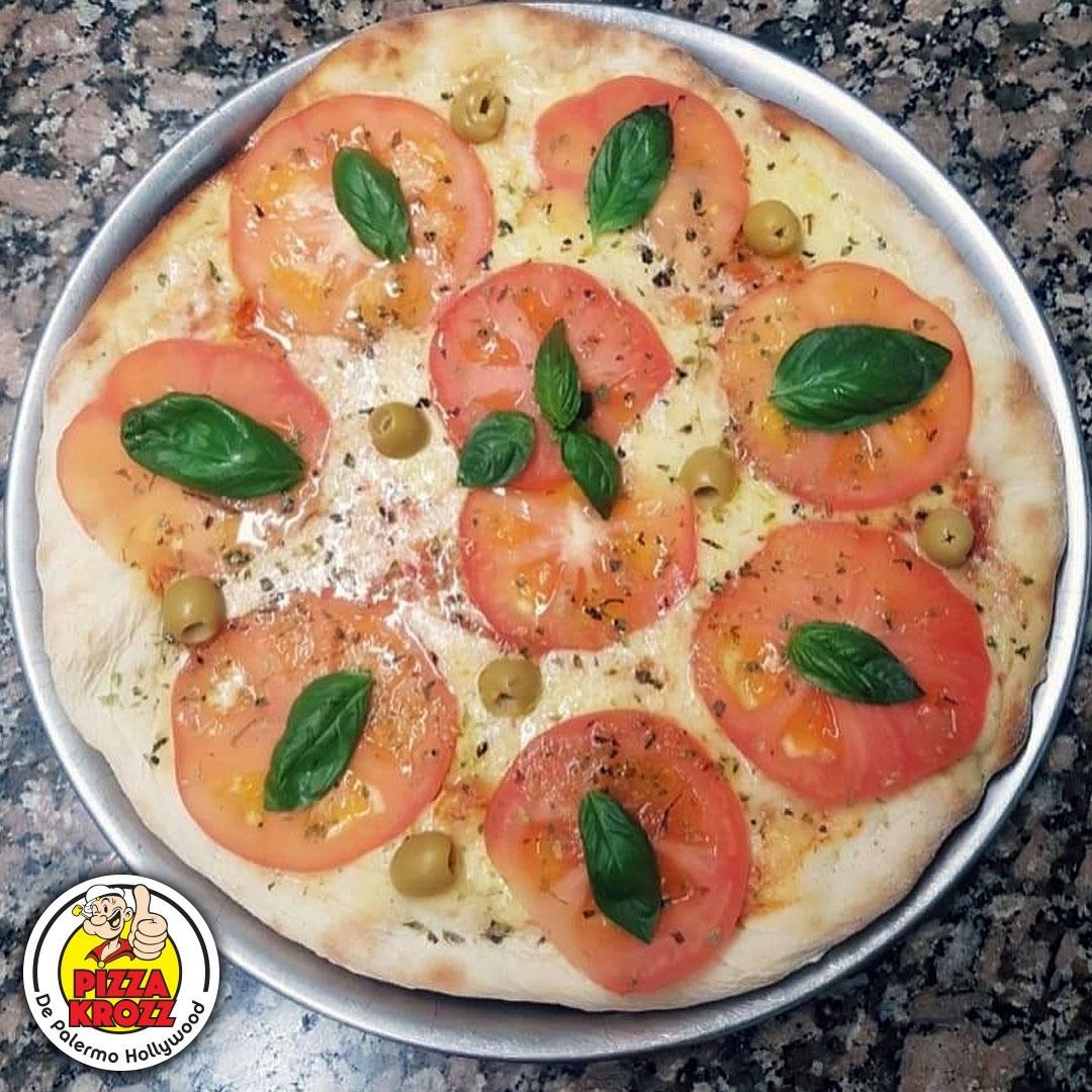 Una pizza redonda cubierta con rodajas de tomate, hojas de albahaca y aceitunas verdes