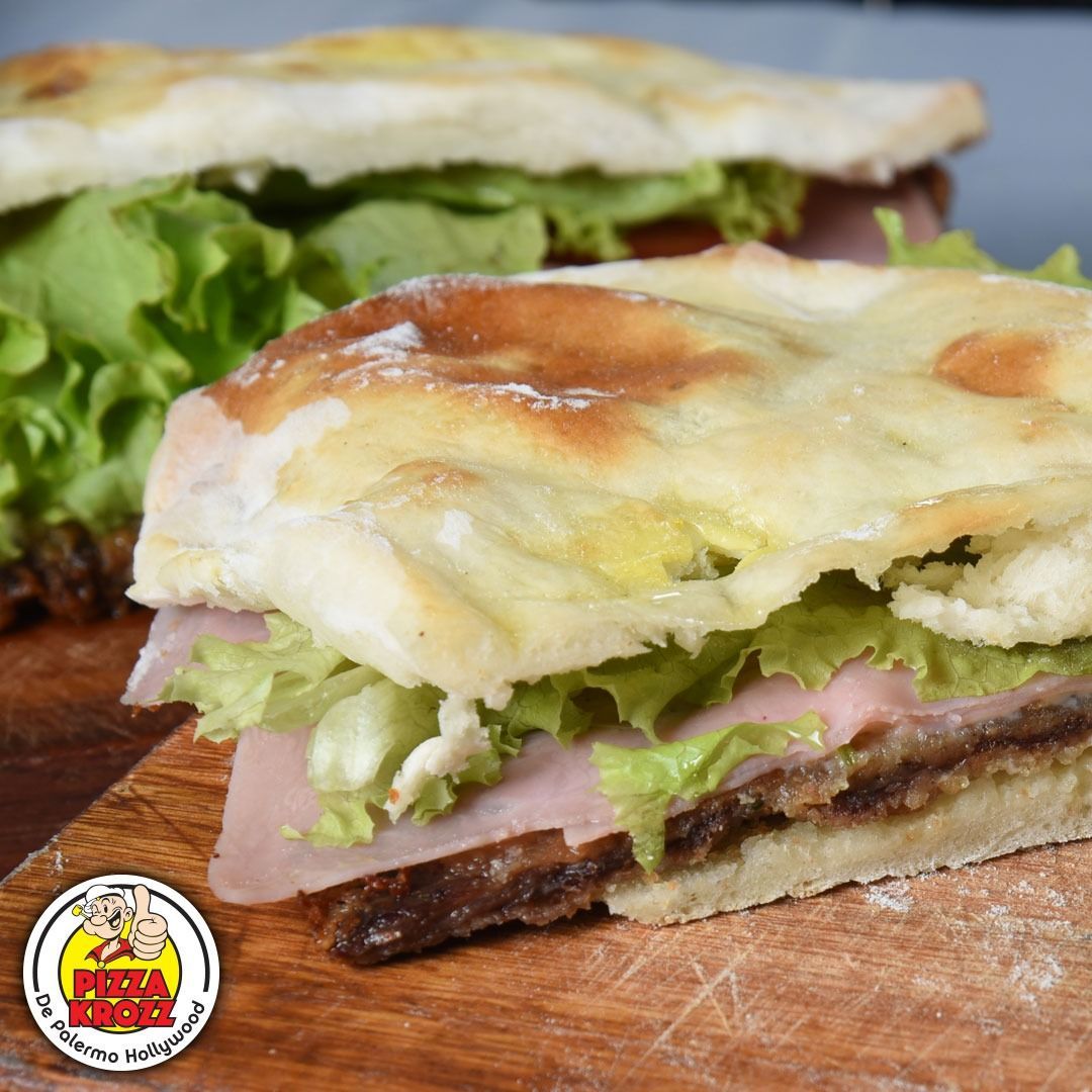 Dos rebanadas de sándwich de jamón, queso y lechuga sobre una tabla de madera