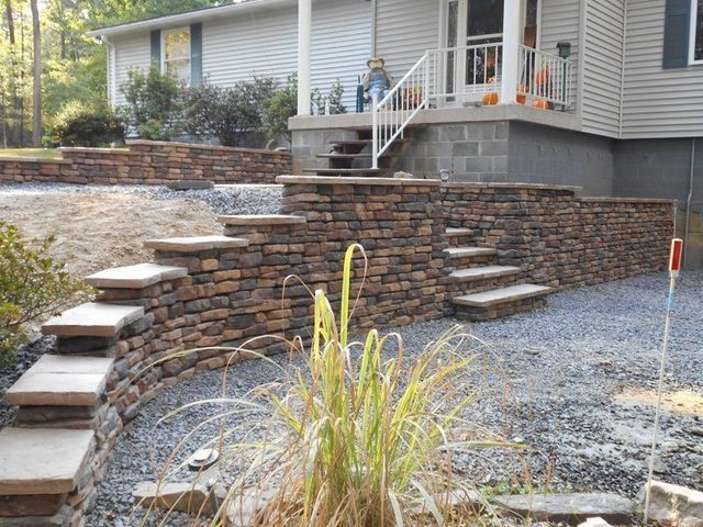 A house with a stone wall and stairs in front of it.