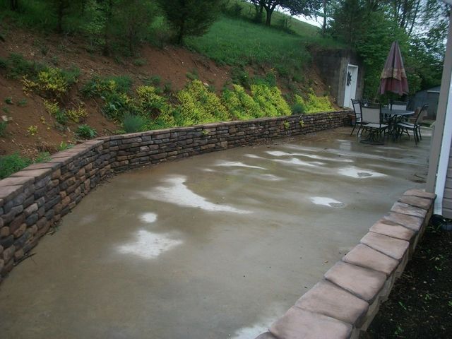 A stone wall surrounds a patio with a table and chairs.