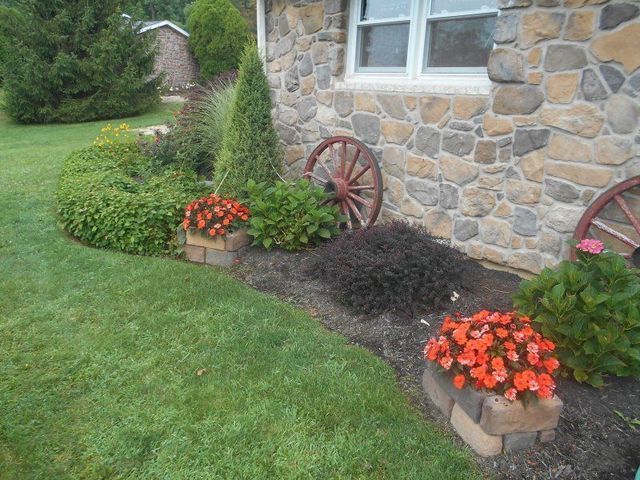 A Stone House with A Wagon Wheel and Flowers in Front of It