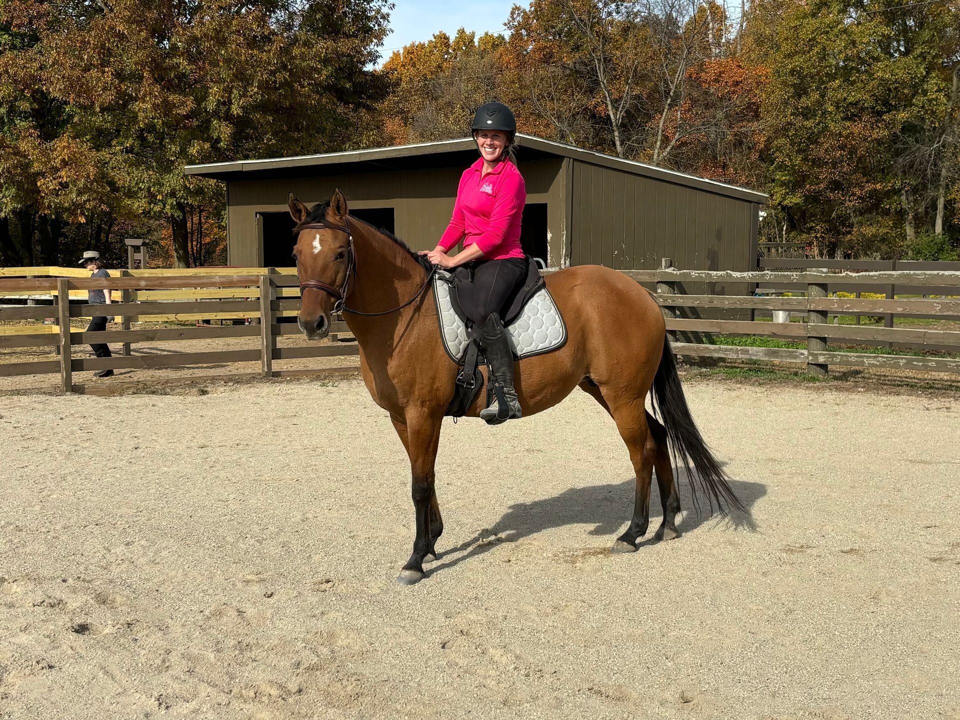 A woman is riding a brown horse in a fenced in area.