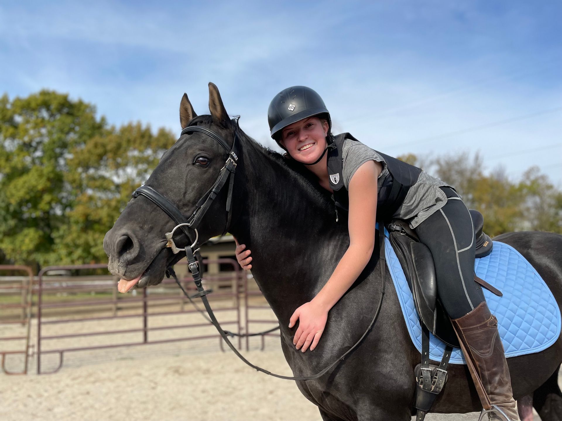 A woman is riding a black horse with a blue saddle.