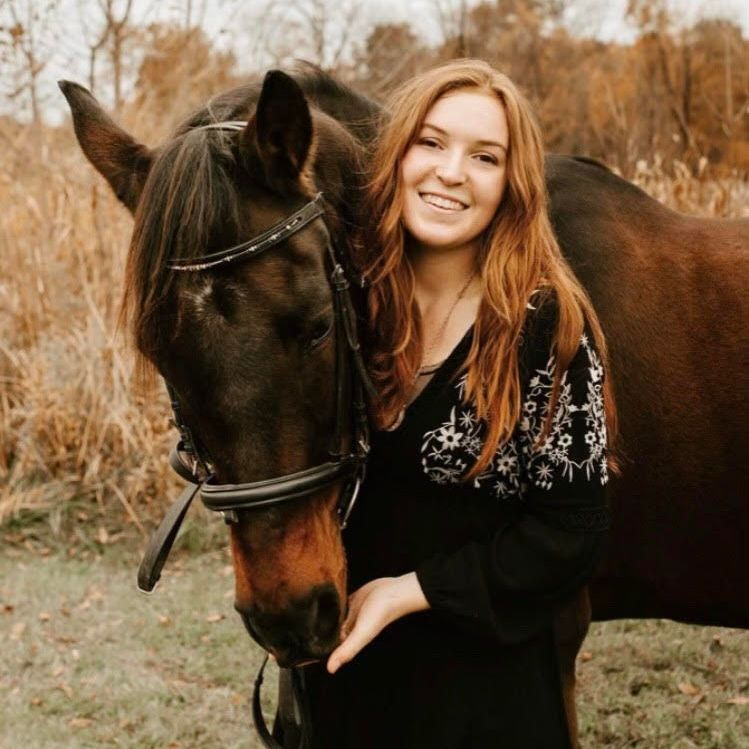 A woman is standing next to a brown horse in a field.