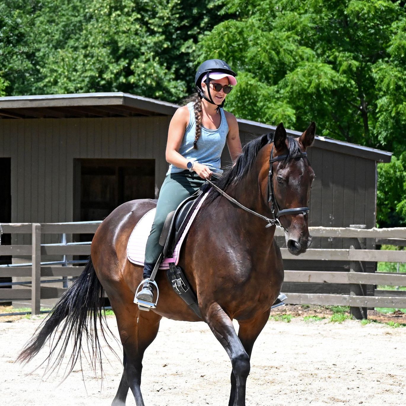 A woman wearing a helmet and sunglasses is riding a brown horse