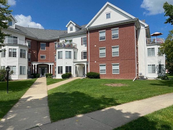a large red brick apartment building with white trim and a lush green lawn in front of it .