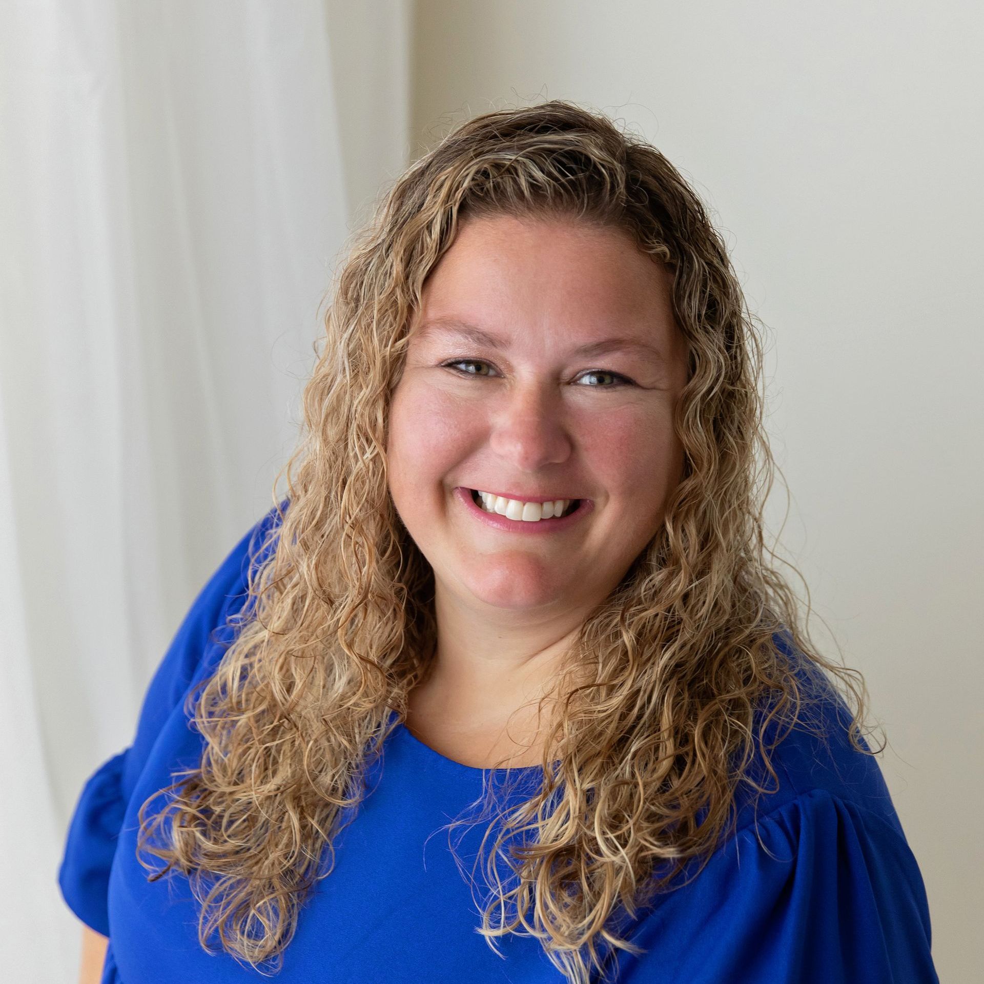 a woman with curly hair wearing a blue shirt smiles for the camera