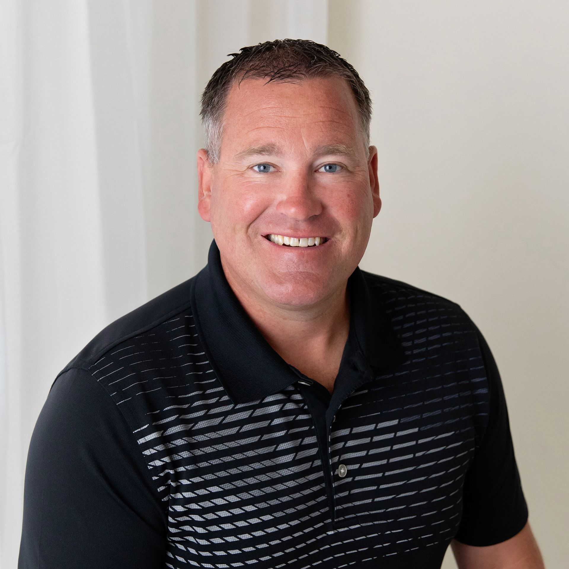 a man wearing a black and grey polo shirt smiles for the camera