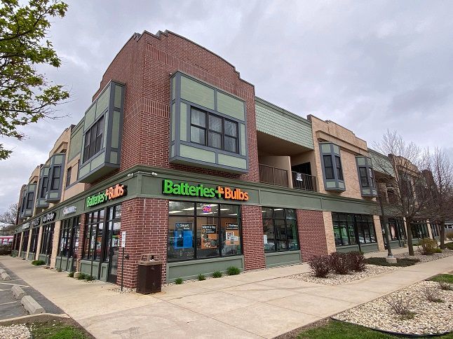 a brick building with a green sign that says batteries + bulbs on it .