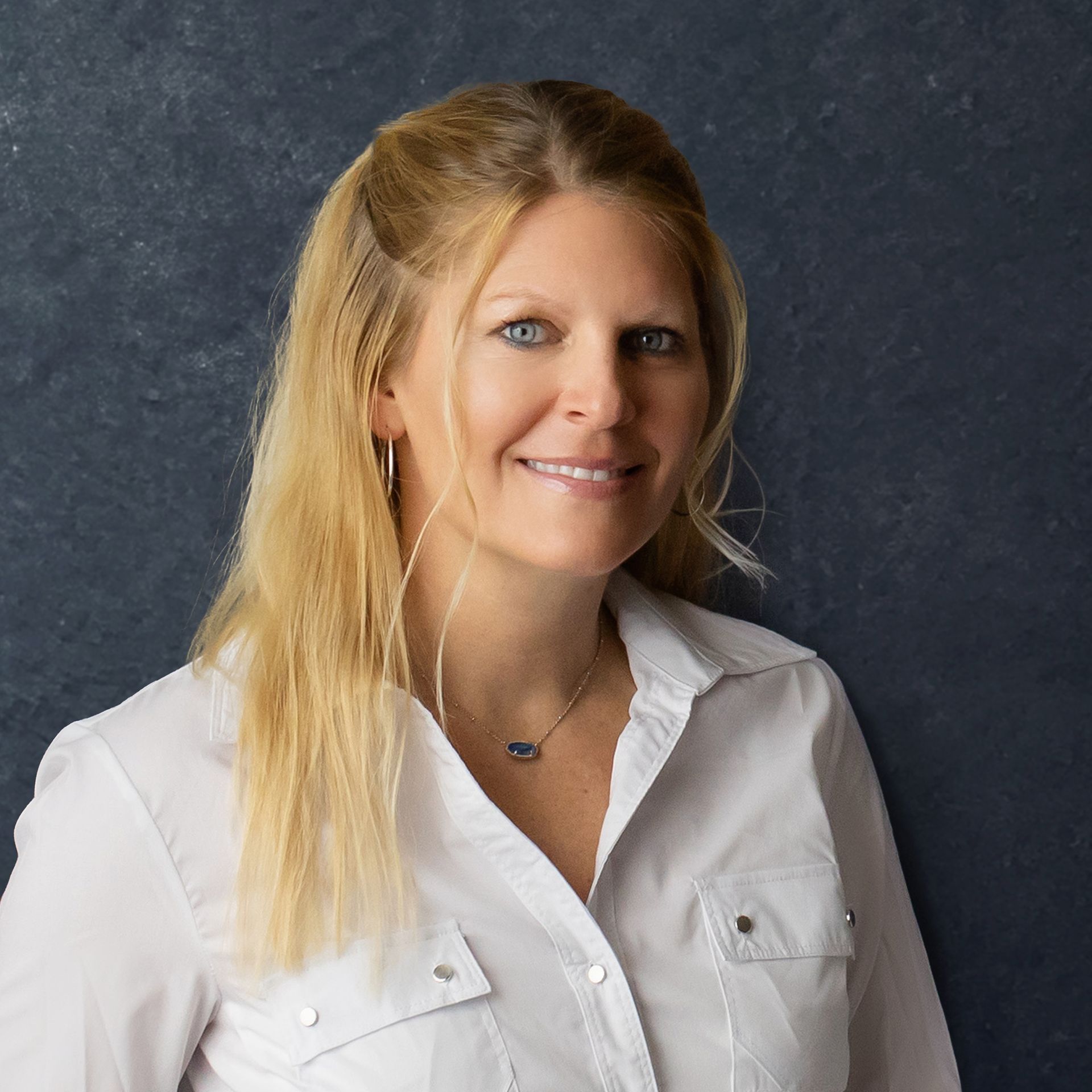 a woman wearing a white shirt and a blue necklace smiles for the camera