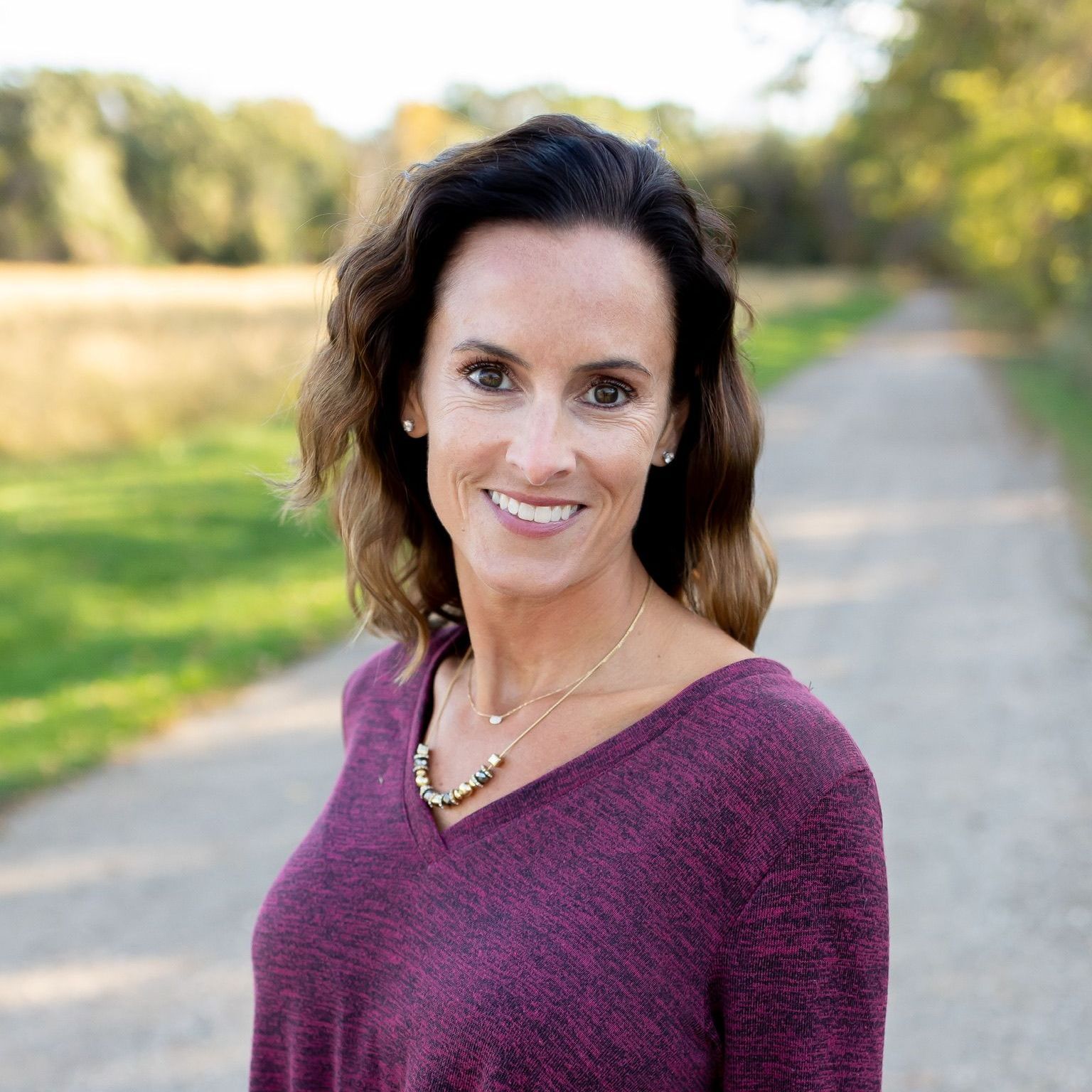 a woman wearing a purple sweater and a necklace smiles for the camera