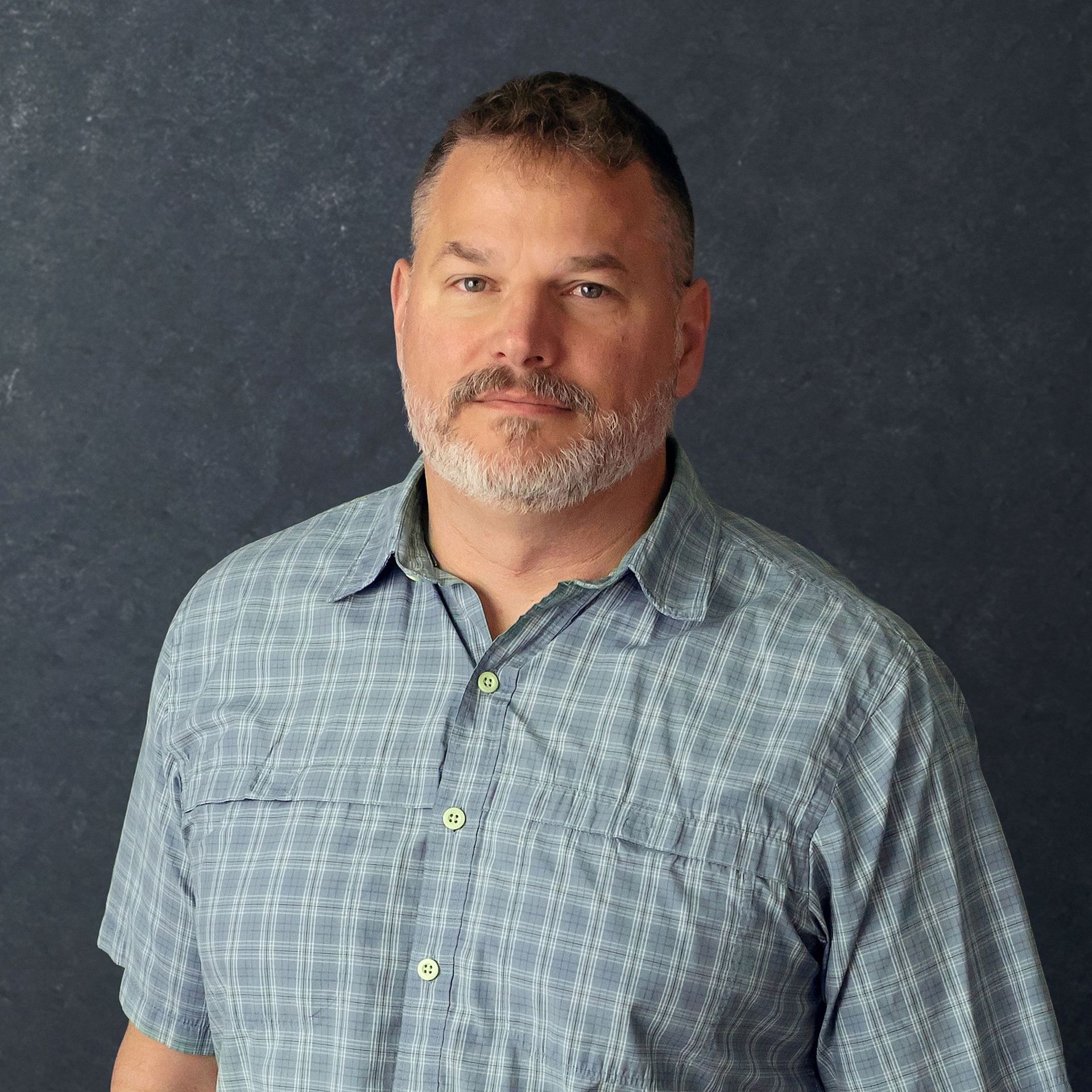 a man with a beard is wearing a blue plaid shirt