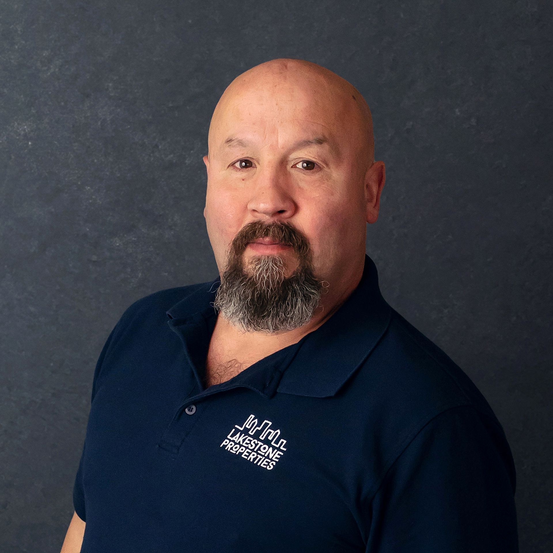 a man with a beard wears a blue shirt that says lakestone properties