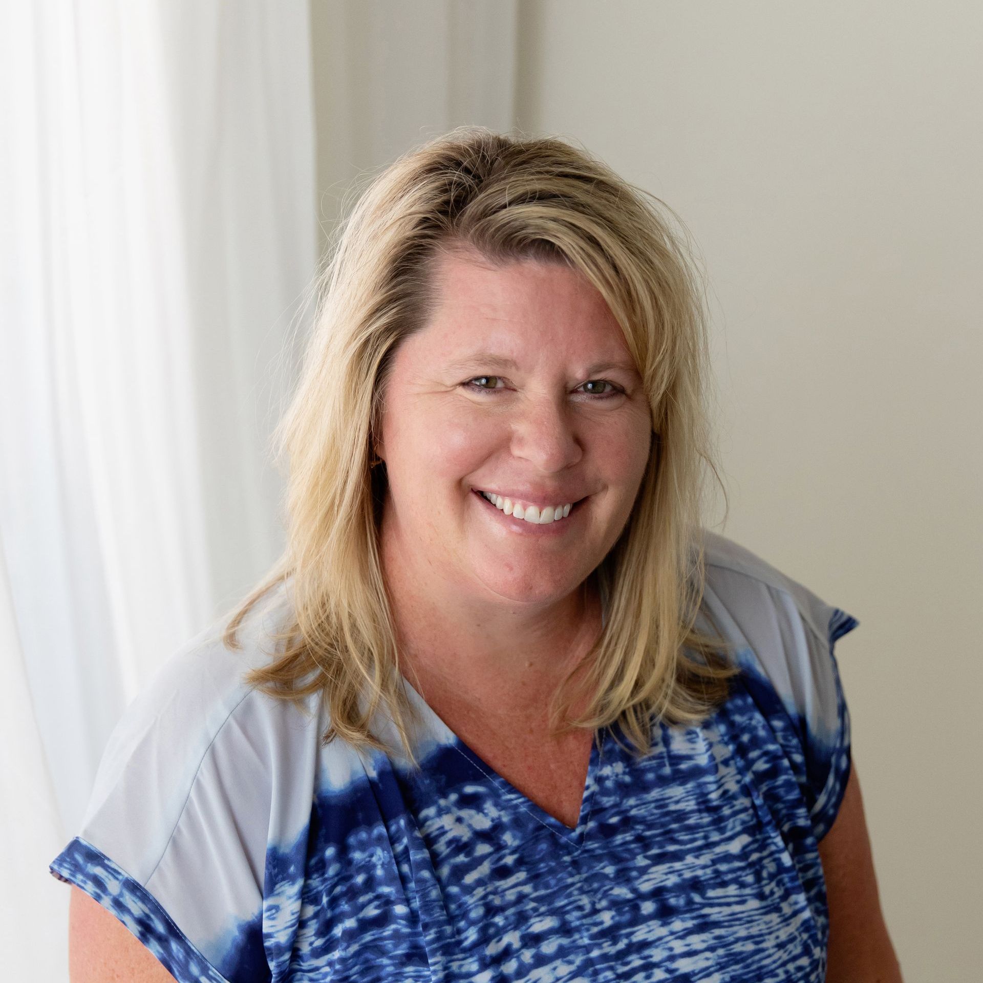 a woman wearing a blue tie dye shirt smiles for the camera